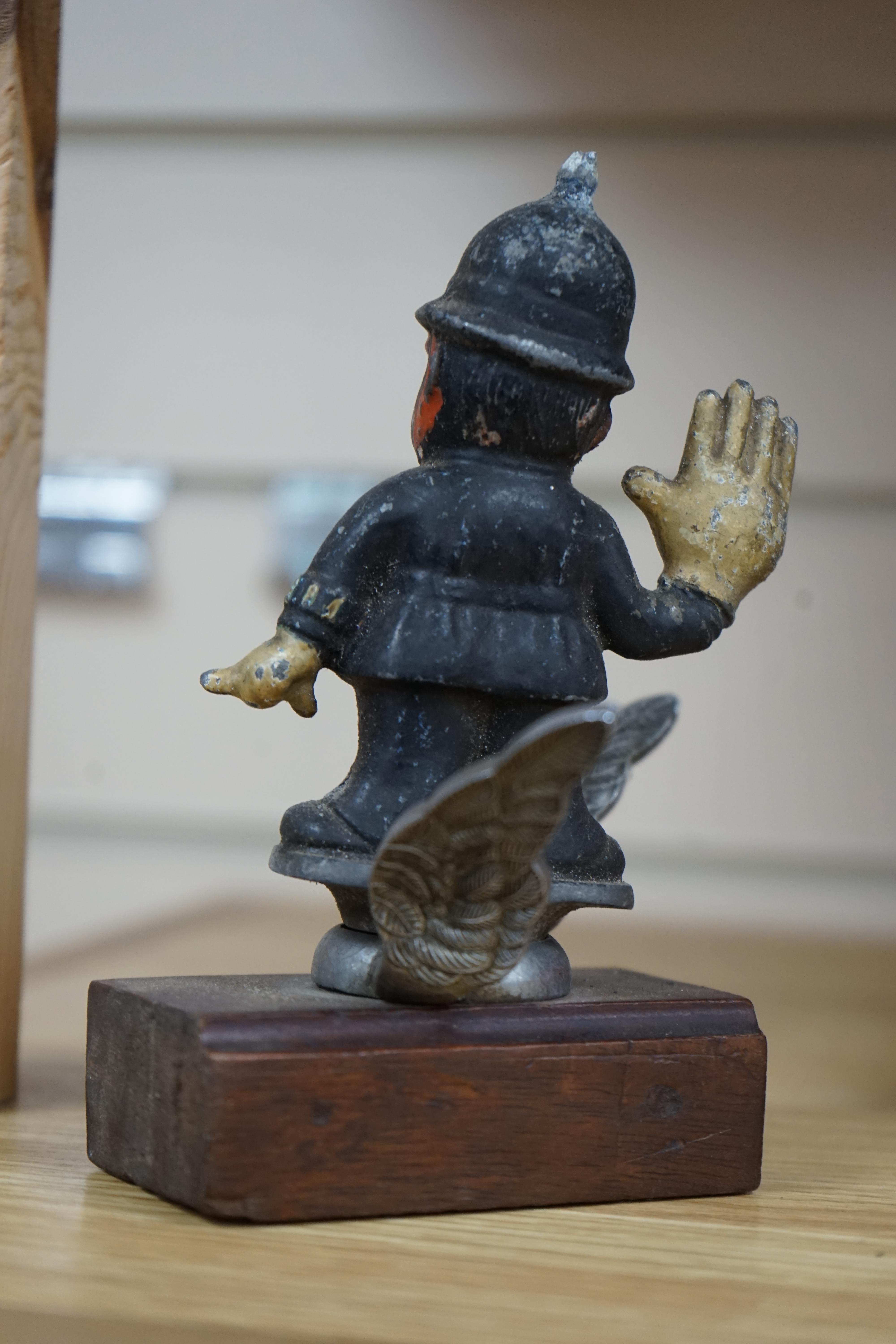 A cold painted cast aluminium car mascot in the form of a caricature of a policeman on associated chromed wings, mounted on a wooden block, policeman 11cm high. Condition - poor to fair.